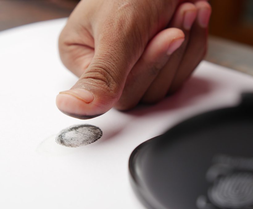 person hand putting black fingerprints on a paper close up ,